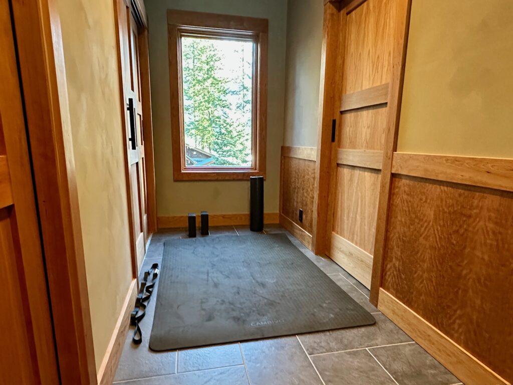 Yoga mat, blocks, and strap set up in Pinehaven’s hallway with treetop views through large window