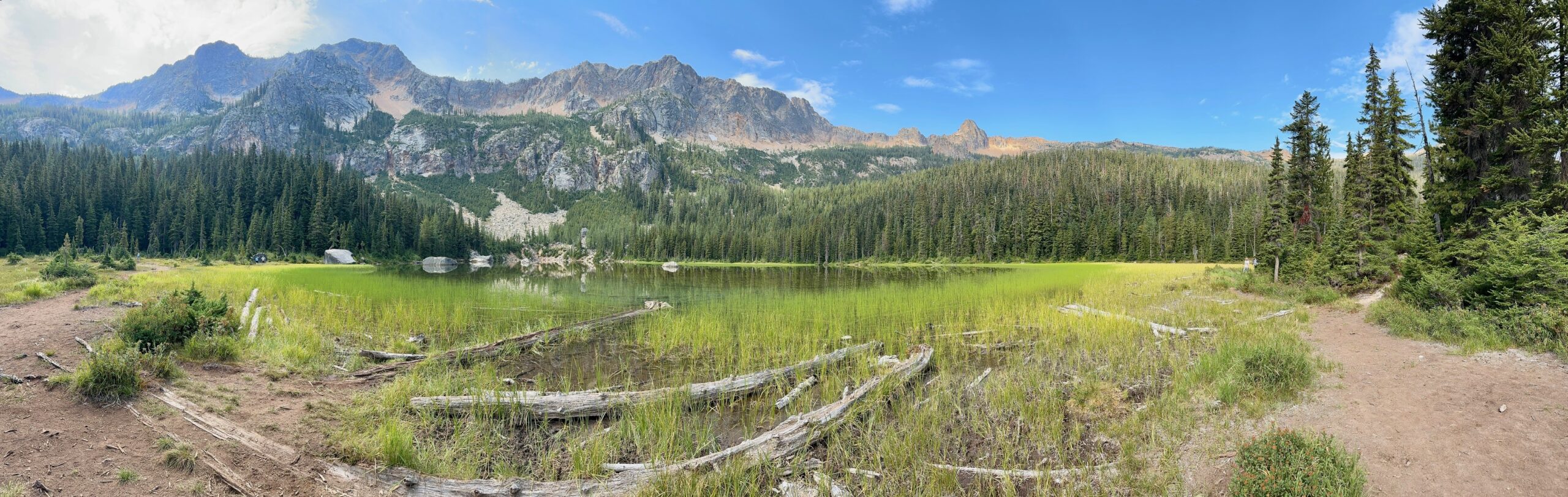 Panoramic view of Cutthroat Lake near Washington Pass, reflecting surrounding mountains in calm green water.