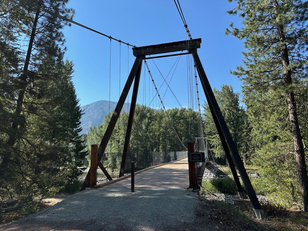 Methow Community Trail suspension bridge crossing the Methow River amid bright summer foliage.